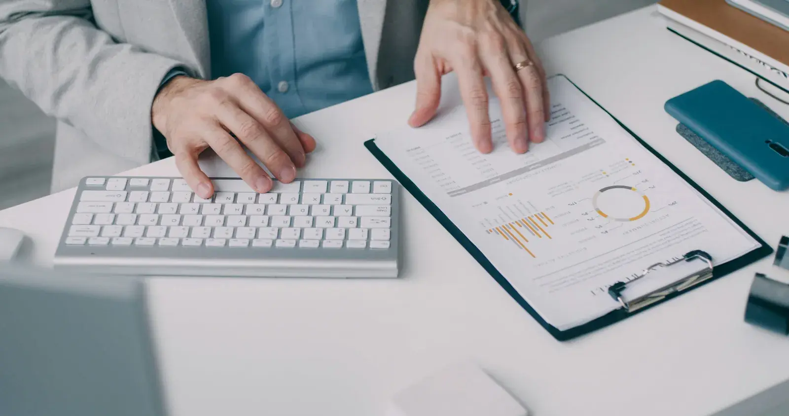 Hands at a keyboard beside a clipboard of printed financial charts and budget figures
